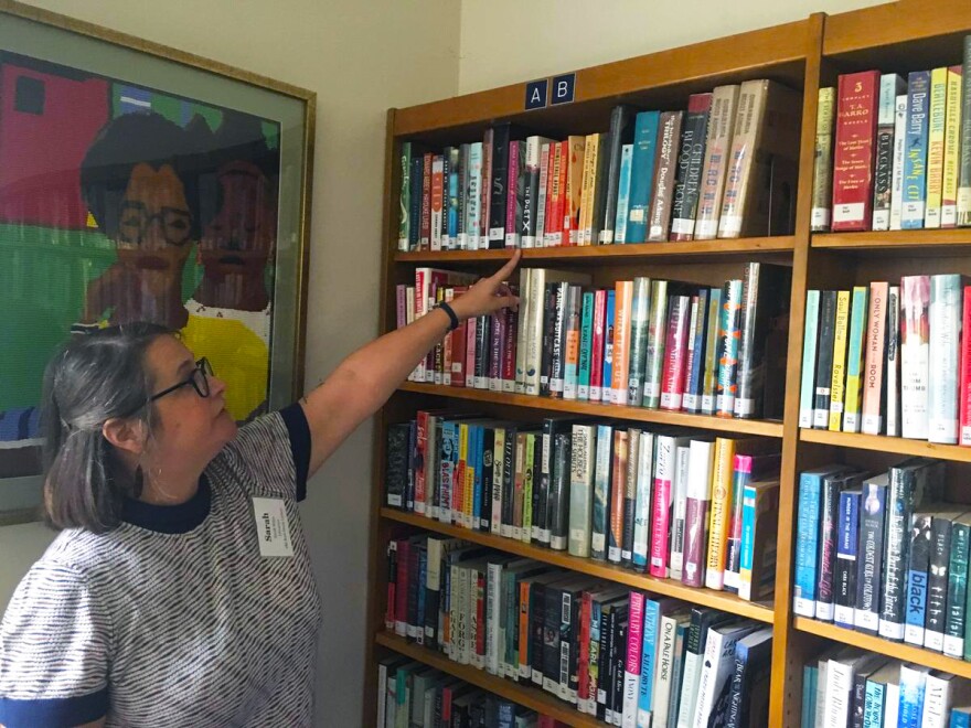 A person points to a top shelf of books in a library