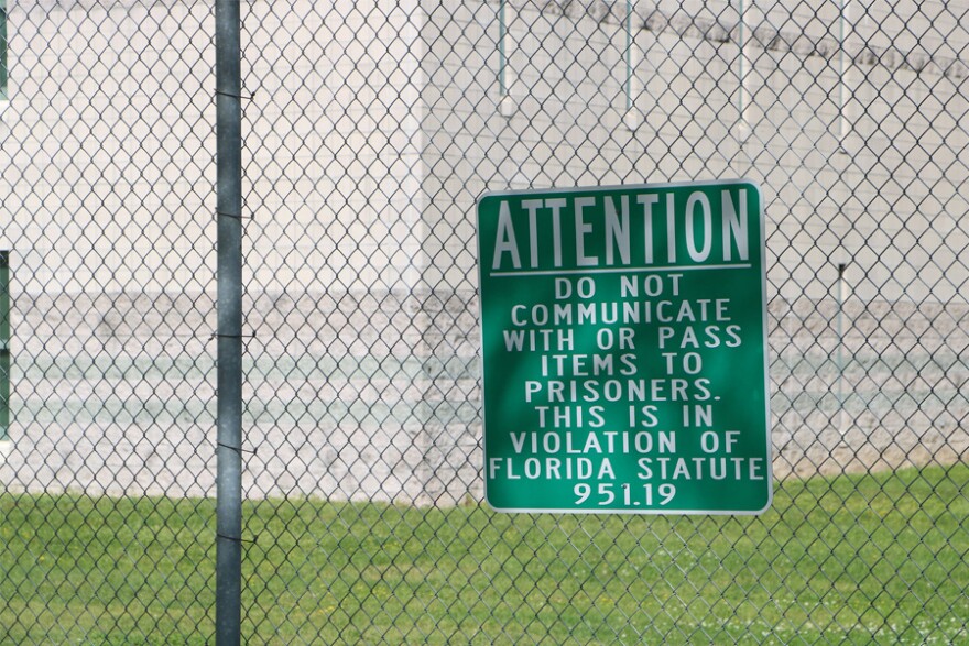 a green sign hangs on a fence warning guests not to communicate or hand prisoners anything