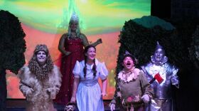 Dorothy, the Cowardly Lion, Scarecrow and Tinman on the yellow brick road as the good witch, Glinda, watches over them.