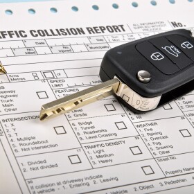 black car key with a traffic collision report and blue pen