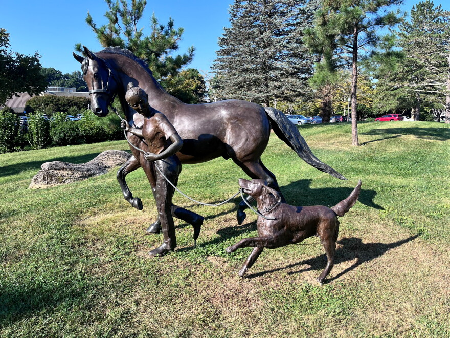Statue of a girl walking a horse alongside a running dog.