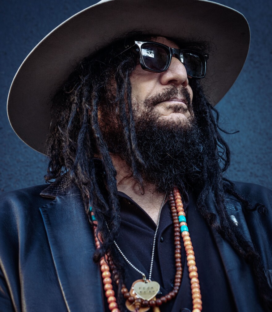 Man with beard and long hair wears sunglasses and a hat. Close up profile shot of him as he stares into the distance. 