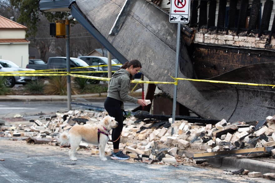 A woman walking her dog looks over a pile of bricks from the collapsed façade of Texas French Bread.