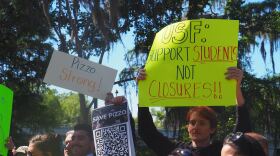 Standing in a park, people hold signs against closing Pizzo Elementary