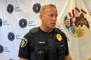 Police officer in security vest with two-way radio and body camera attached as he stands in front of a flag of Illinois