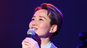 A Japanese woman with short hair on stage holding a microphone.