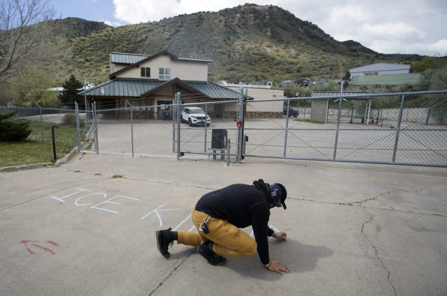 A confirmer writes “ICE KIDNAPS KIDS” with chalk outside the ICE facility in Durango.