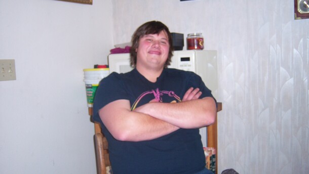 A smiling young man sits in a chair with his arms crossed.