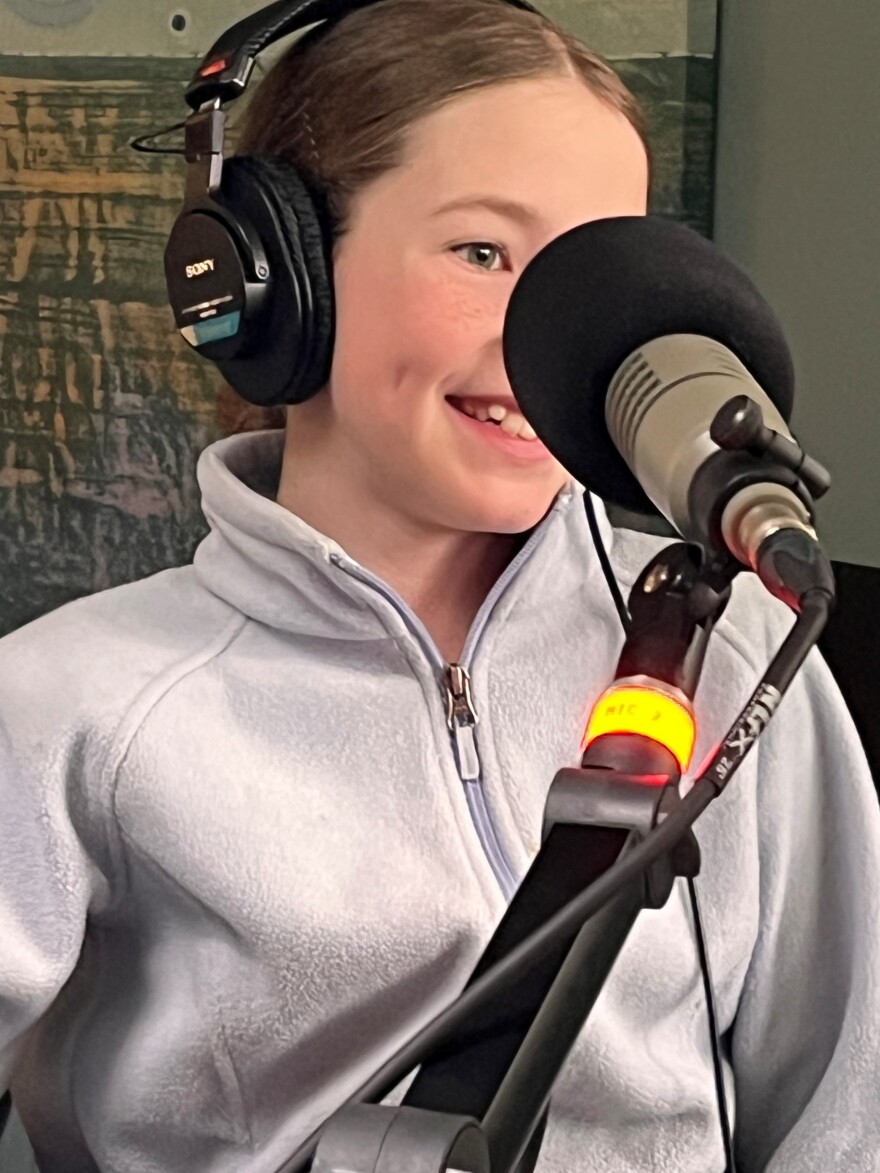 A young girl smiles behind the microphone at KAXE.