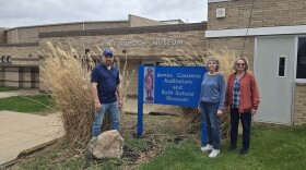 Chris Hagerman, Susan Hagerman and Michelle Allen standing next to a sign with the James Couzens Auditorium and Bath School Museum, in front of the Bath School Museum entrance