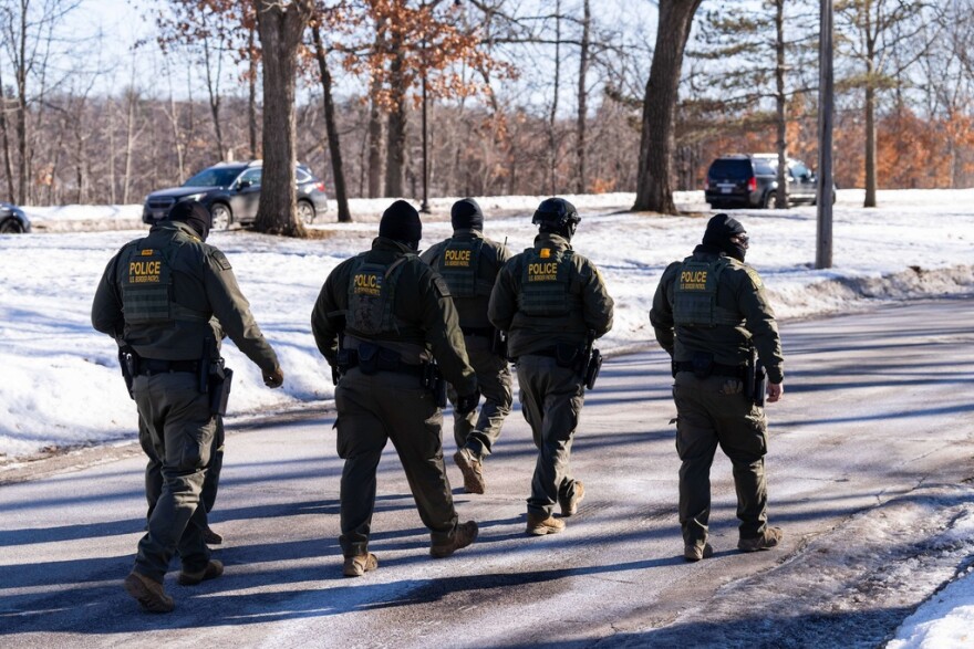 Five people in military outfits walk on an icy street.