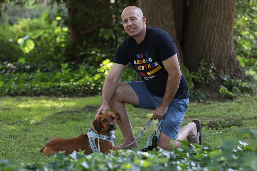Chris Fitzgerald, former director of Rochester Animal Services, kneels in his front lawn and rests his hand on the head of a small brown dog named Mikey, which he adopted in March from a rescue organization. Fitzgerald resigned in February 2024, after nearly 24 years on the job.