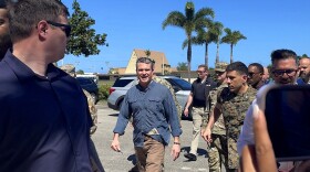 U.S. Defense Secretary Pete Hegseth in a blue shirt and brown pants walks with an extensive security detail at Andersen Air Force Base, Guam.