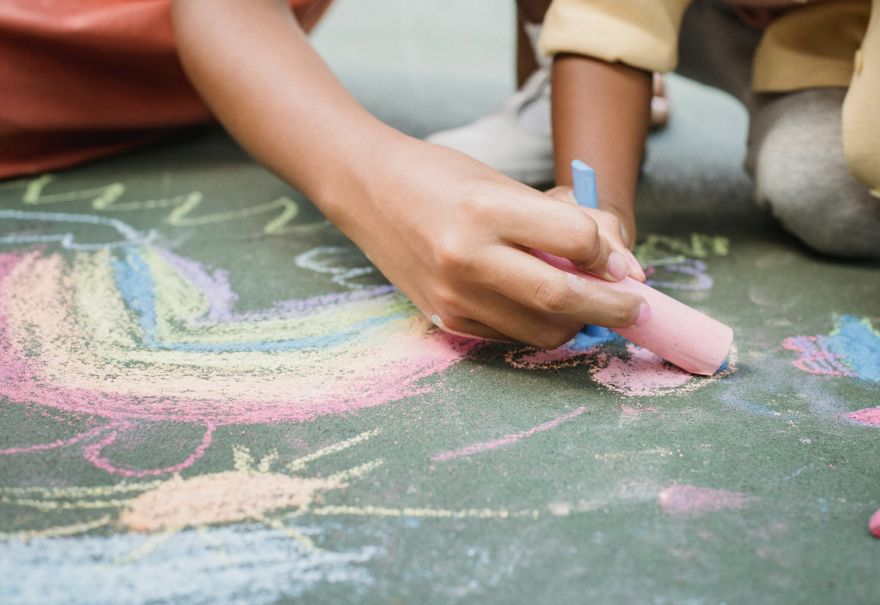 Close-up of two people drawing colorful chalk art on the pavement.