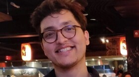 Headshot of Gustavo Sagrero. He is sitting in a restaurant while looking toward the camera and smiling.