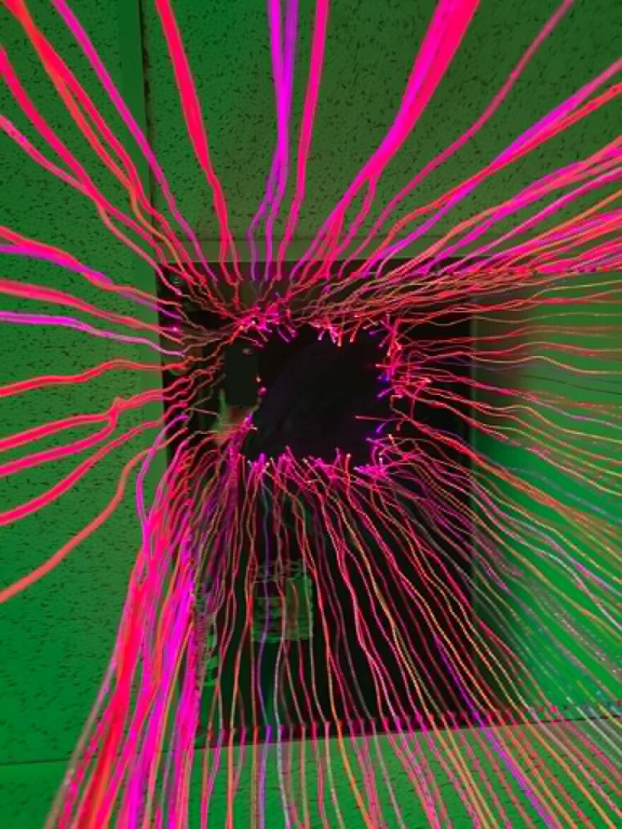 Pink, orange and purple lights shine in fiber string lights from the ceiling in a mesmerizing effect, almost like a neon jellyfish hanging from the ceiling.