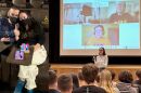 Left image: Tim and Emily Lowrey at a movie. Emily shared with BTPM NPR: "one year after diagnosis during COVID lock-down at a movie theatre in downtown Buffalo. We went with two pharmacist friends and had the entire theatre to ourselves. Such a treat." Right image: Emily Lowrey speaks in front of an auditorium of students at Iroquois High School in May 2026.