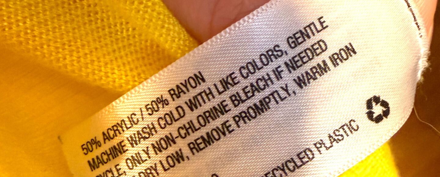 The care label inside of a garment made in China is shown, reflecting it's made up of a mixed blend of acrylic and rayon.