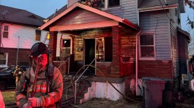 An unnamed firefighter stands before a burnt house.