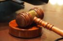 A wooden gavel resting on a stand on a wooden table.