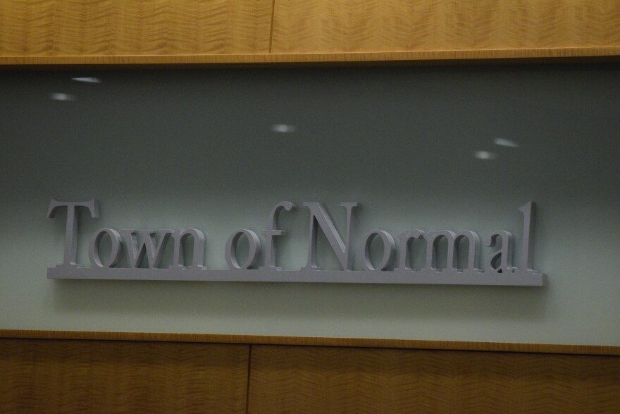 In gray lettering reads, 'Town of Normal' with a gray background, against a wooden wall.