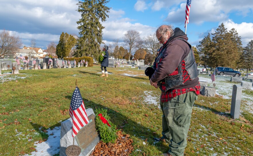 Brian Dougherty places his first wreath at the memorial stone of the Missing in Action Veteran Wayne Wolfkeil. Dougherty also wears a bracelet in rememberance of Wolfkeil.