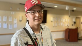 A young man smiles at the camera. He's wearing a red hat with a logo on it and a colorful shirt.