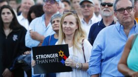 Iris Schaen, center, holds a sign as she listens to speakers during an interfaith vigil against anti-semitism and hate at the Holocaust Memorial, Tuesday, Oct. 30, 2018, in Miami Beach, Fla. 