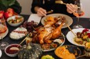 A close-up picture of a Thanksgiving meal on a table, with a turkey, squash, cheese and cranberry sauce.