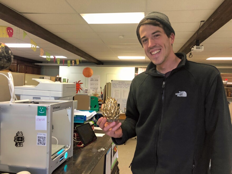 Spark Coordinator Ezra Ranz holds up a pineapple he made in the 3-D printer beside him.