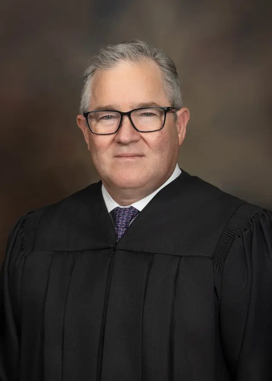 A man with grey hair and dark glasses wearing a judge's robe