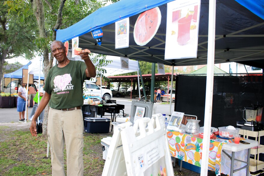 Willie Robinson at his Life In A Bottle vendors tent at Gainesville Farmers Market at Heartwood and South Main Station with a sample of a half pineapple-half watermelon smoothie, September 16, 2022. (Ismara Corea/WUFT News)