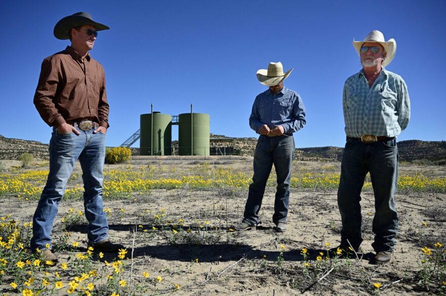 Kaleb Hodgson, Luke Whitley and Richard Hodgson stand in a pasture on the Hodgson ranch. Years ago, the well tanks behind them leaked and flooded the pasture with produced water and oil. (Jerry Redfern/Capital & Main)
