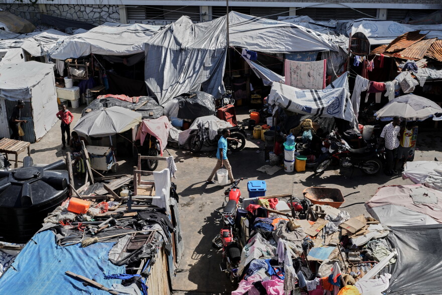 A man carries buckets of water where families displaced by gang violence are living in Port-au-Prince, Haiti, Wednesday, Aug. 12, 2026.