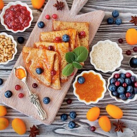 Wooden board with gluten-free crepes surrounded by jams and fruits