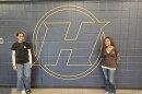 Haslett High School students Aikem Gill (left) and Nanaty Assefa (right) stand next to Haslett High School logo painted on a school wall