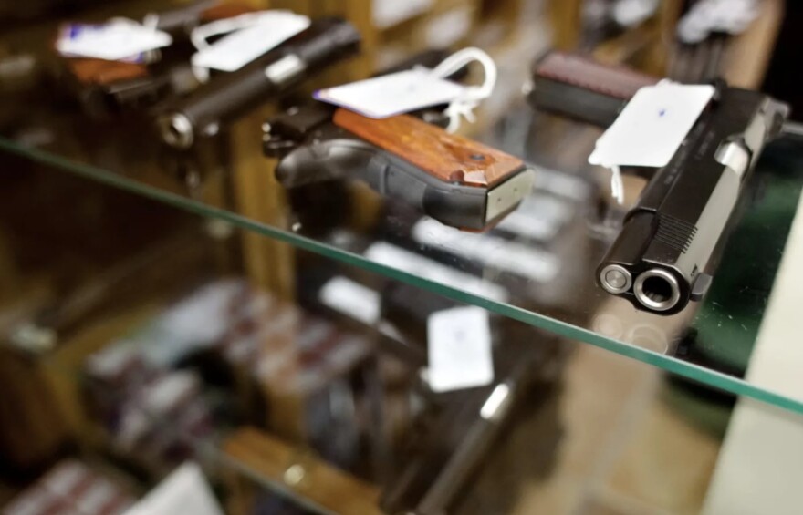 Different guns lay on glass shelves in a store.