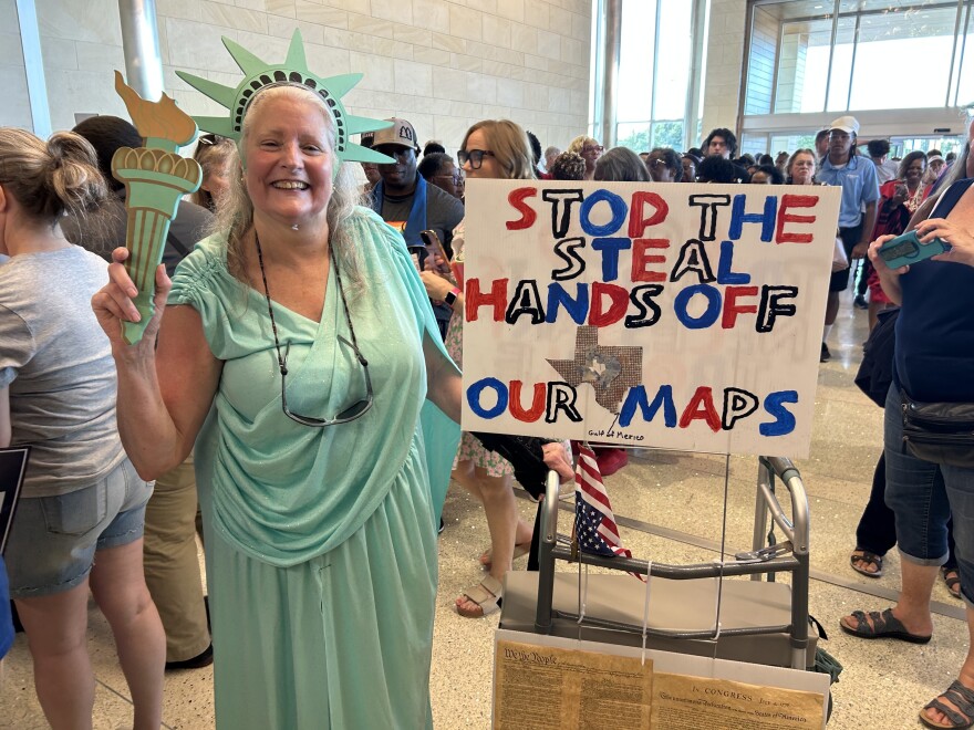 A photo of a woman wearing a Lady Liberty costume in a crowded theater lobby, with a sign that says "Stop the steal, hands off our maps."
