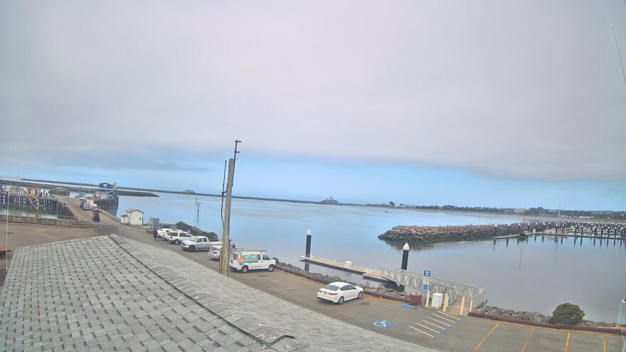 A view of a harbor from on top of a building, stone wave breaks and docks are visible, as well as a parking lot at the bottom of the frame