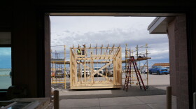 Two students work on the top of a framed, wooden structure outside.
