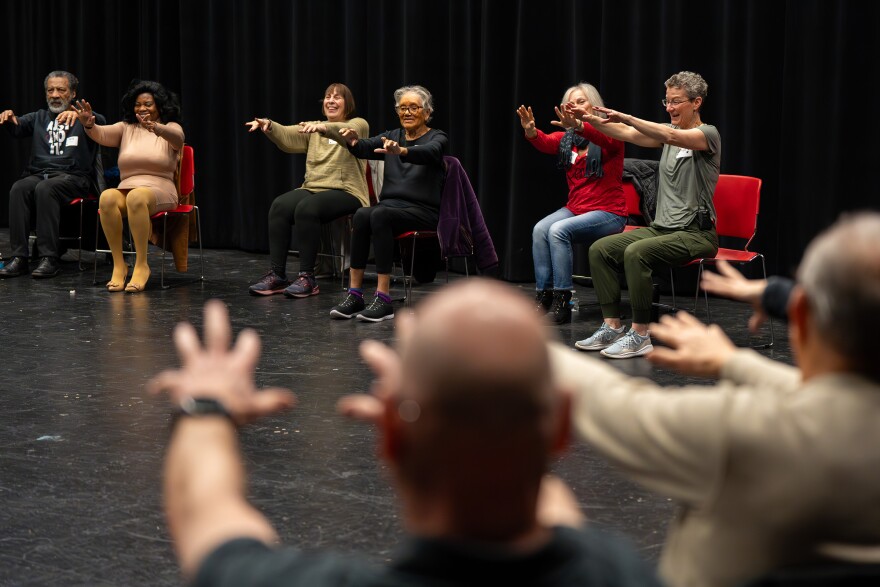 Several older adults in a circle with arms outstretched