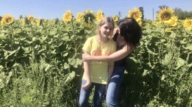 A mother and her teenaged daughter hug in a field of sunflowers