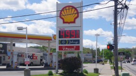 A Shell gas station sign next to a busy road displays the price for gas; $4.99