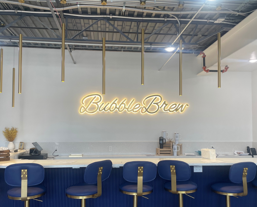 Chairs at a long table with the words "Bubble Brew" glowing on the wall. 