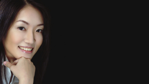 Pianist Yi-Wen Chang is pictured smiling, leaning on her hand, from the left side of the frame, on an otherwise plain black background