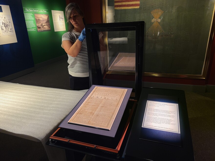 copy of the Declaration of Independence lays in an open display case. a woman is poised to close the case
