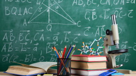 Education and sciences concept - books, molecule model and microscope on the desk in the auditorium, chalkboard background.