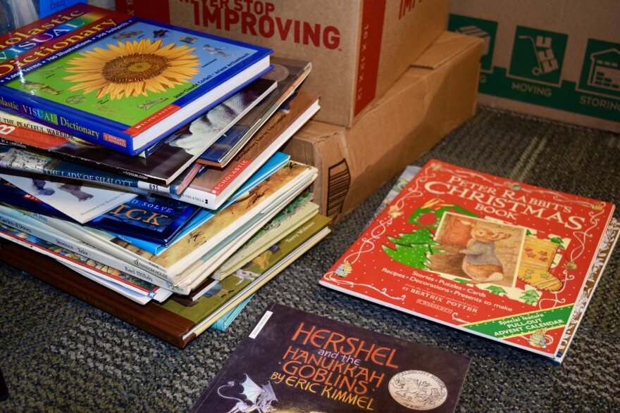 A precarious stack of books as a visual dictionary on top. Next to it on the floor sit "Peter Rabbit's Christmas Book" and "Hershel and the Hanukkah Goblins."