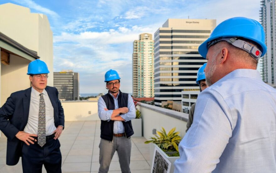 Men in hard hats gather outside on balcony with skyline in the background 