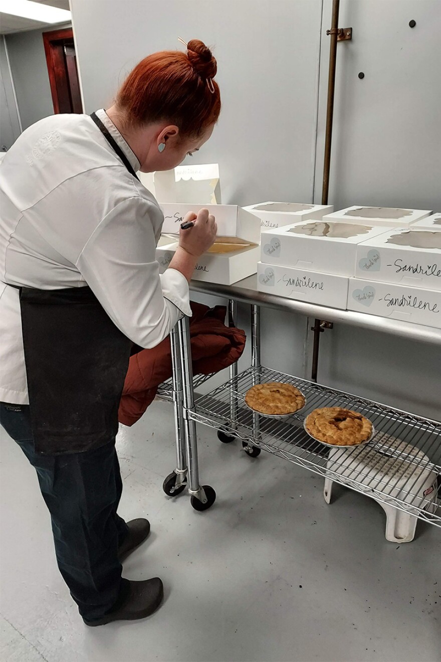 A baker labels a boxes of pie on a rack in a kitchen.
